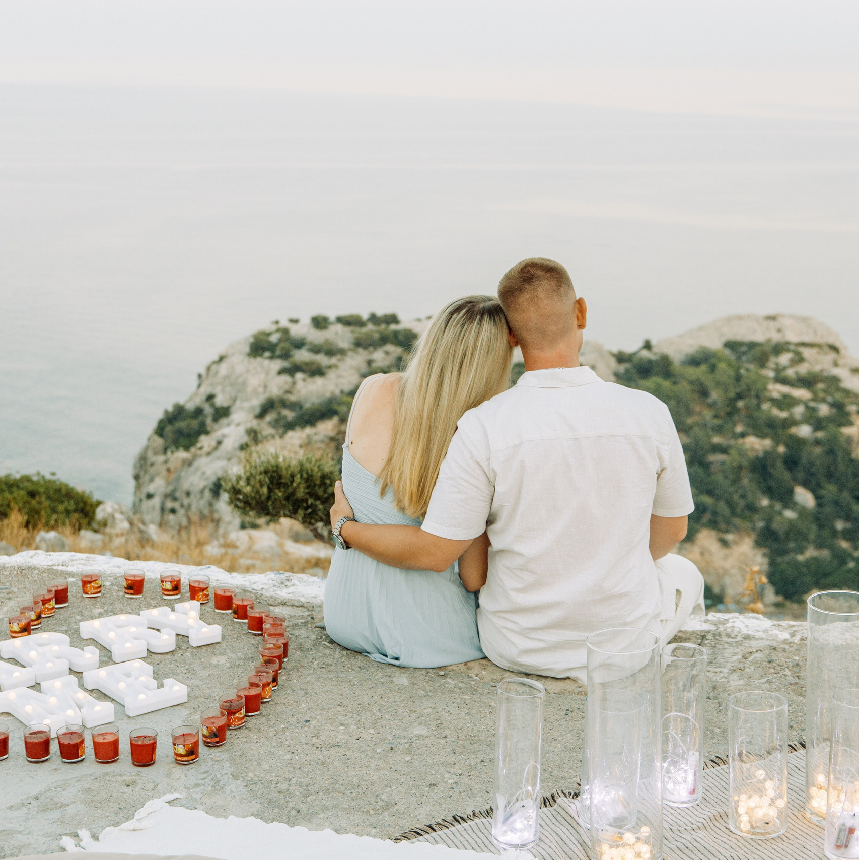 Engagement in Rhodes 💍 engaged couple sitting after the proposal at Profitis Ilias near Faliraki overlooking the Aegean Sea in Greece.