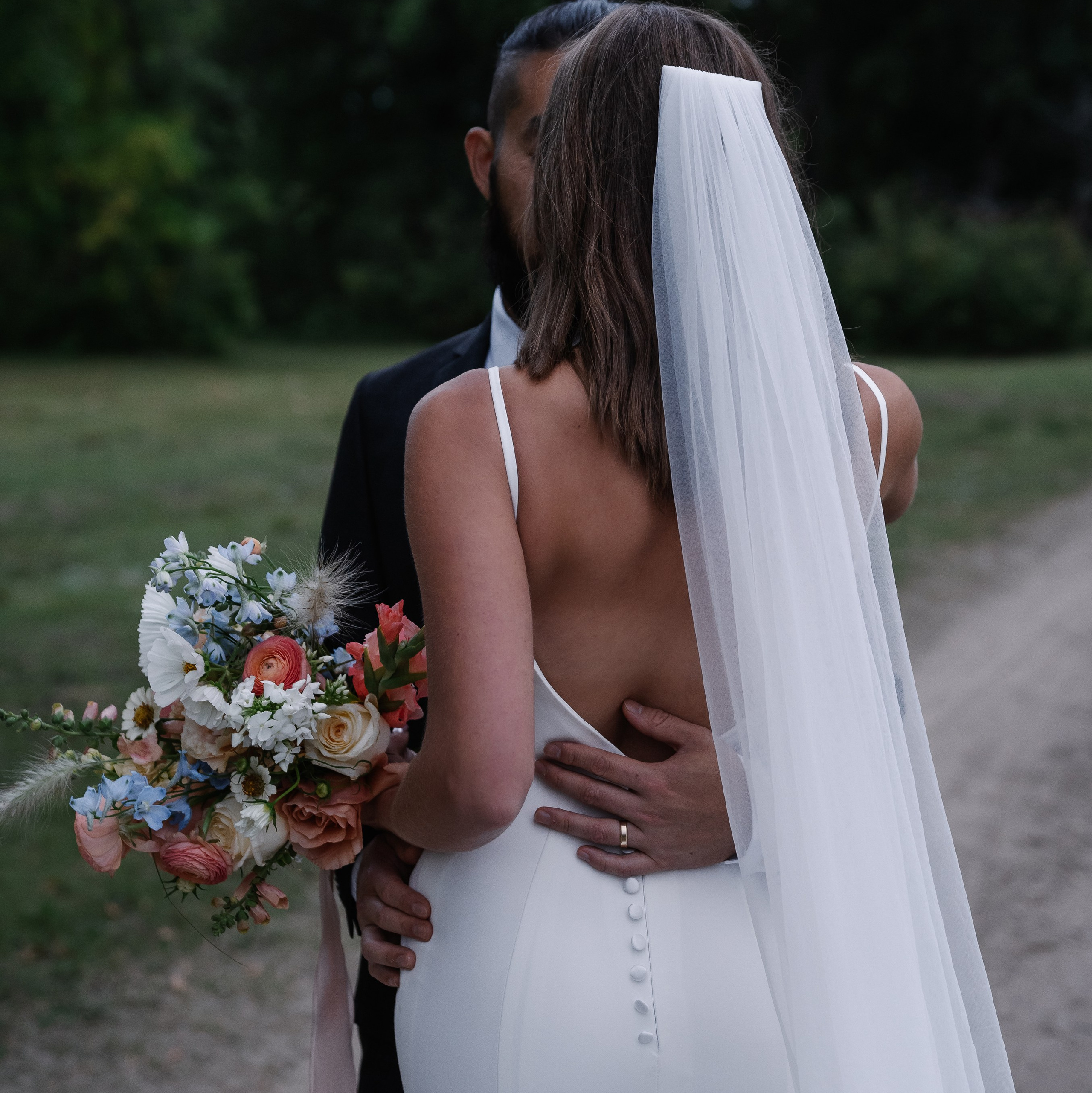 Groom embracing bride, bride holding bouquet and wearing a veil.