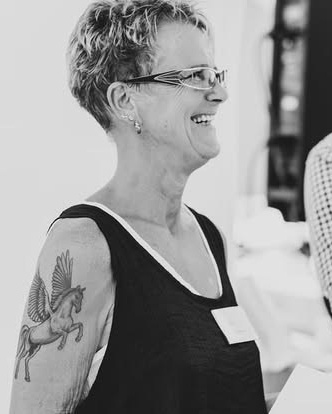 „Fröhliches Porträt von Hochzeitsplanerin Renate auf Rhodos, die lächelnd ein schwarzes Top trägt und ihr Pegasus-Tattoo zeigt.“