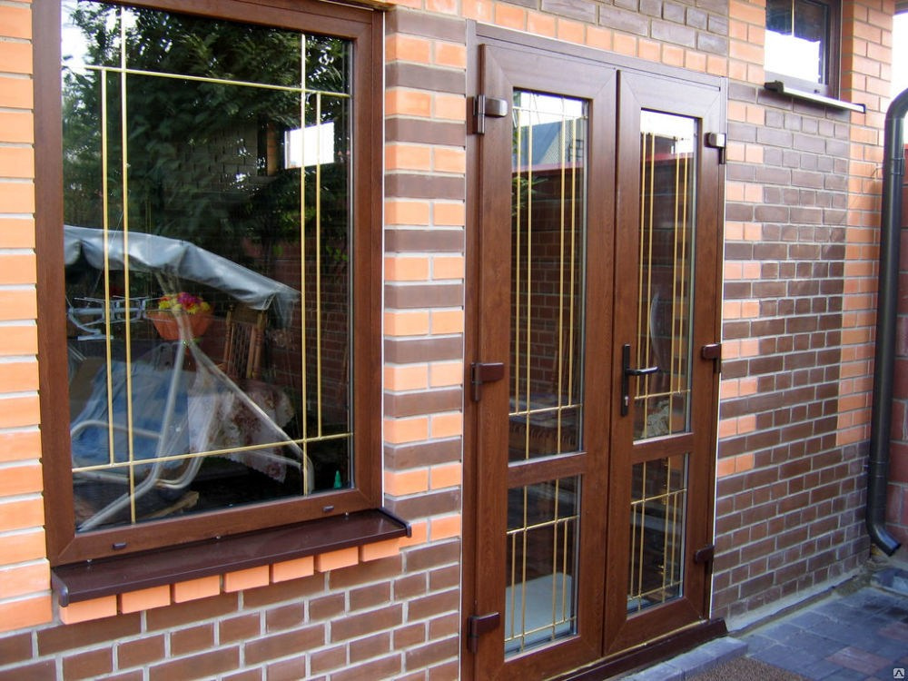 Пластиковая дверь входной группы, вместе с панорамными окнами в ламинации, тонированными стеклопакетами и шпроссами в жилом доме.