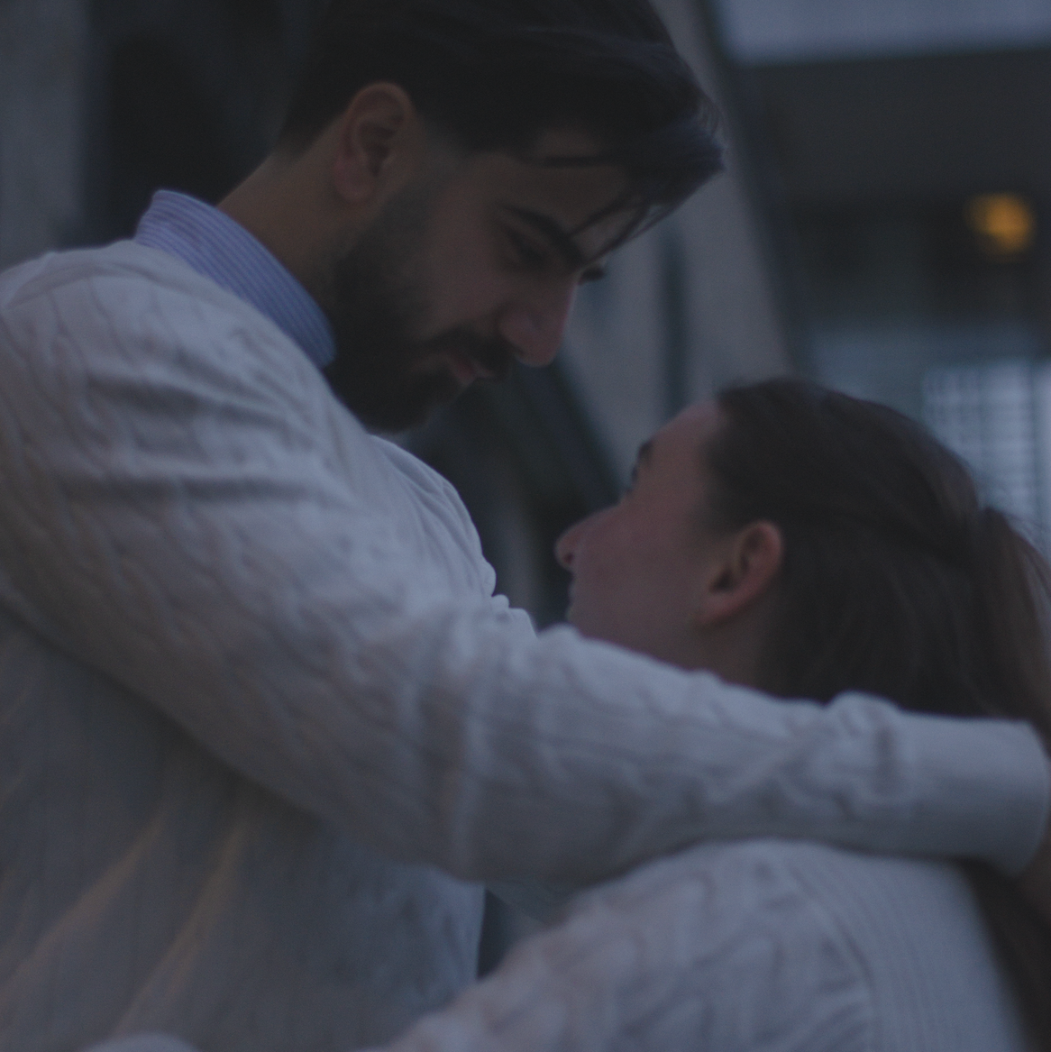 Verliebtes Paar mit dunklen Haaren schaut sich verträumt in die Augen vor urbanem Hintergrund
