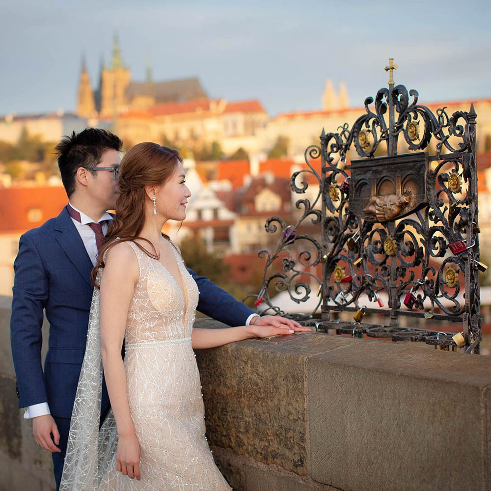 A stylishly dressed couple pause to make a wish at a religious spot atop the Charles Bridge in Prague.