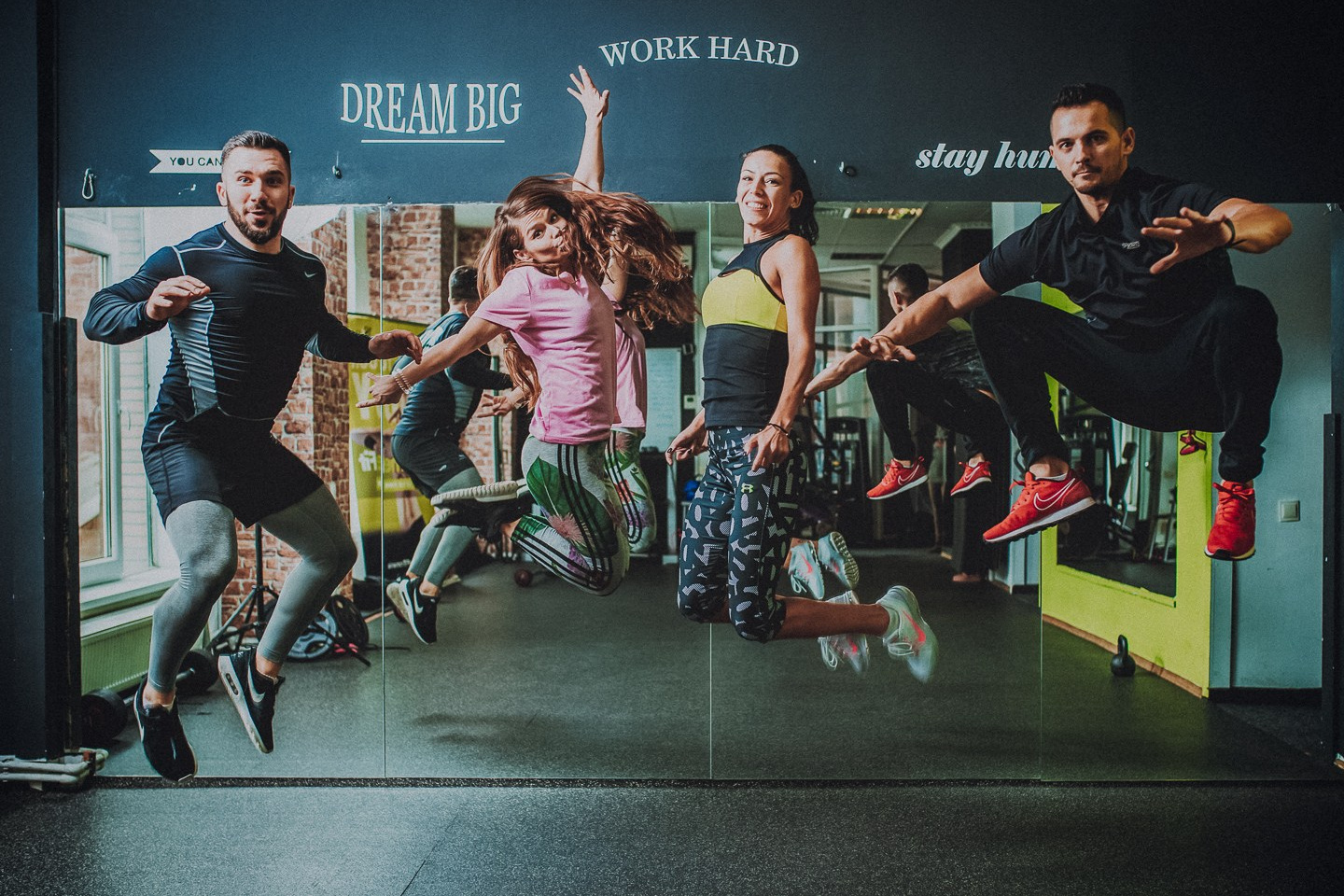 Grup de antrenori de fitness sărind în aer în fața oglinzii cu mesajele Dream Big Work Hard, foto Photosinteza