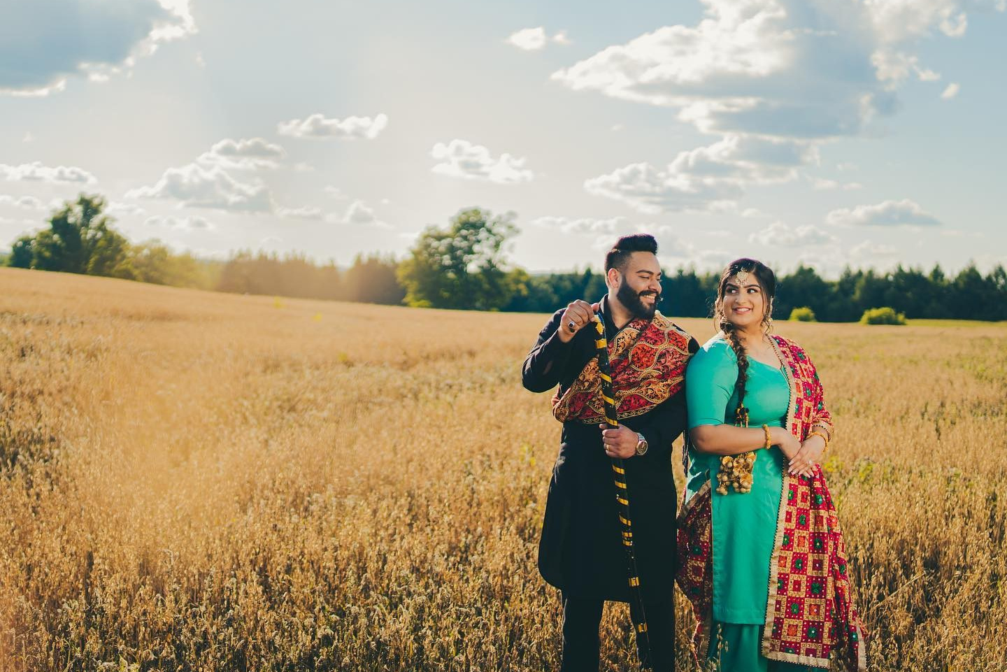 Bride and groom walking through golden wheat field during sunset