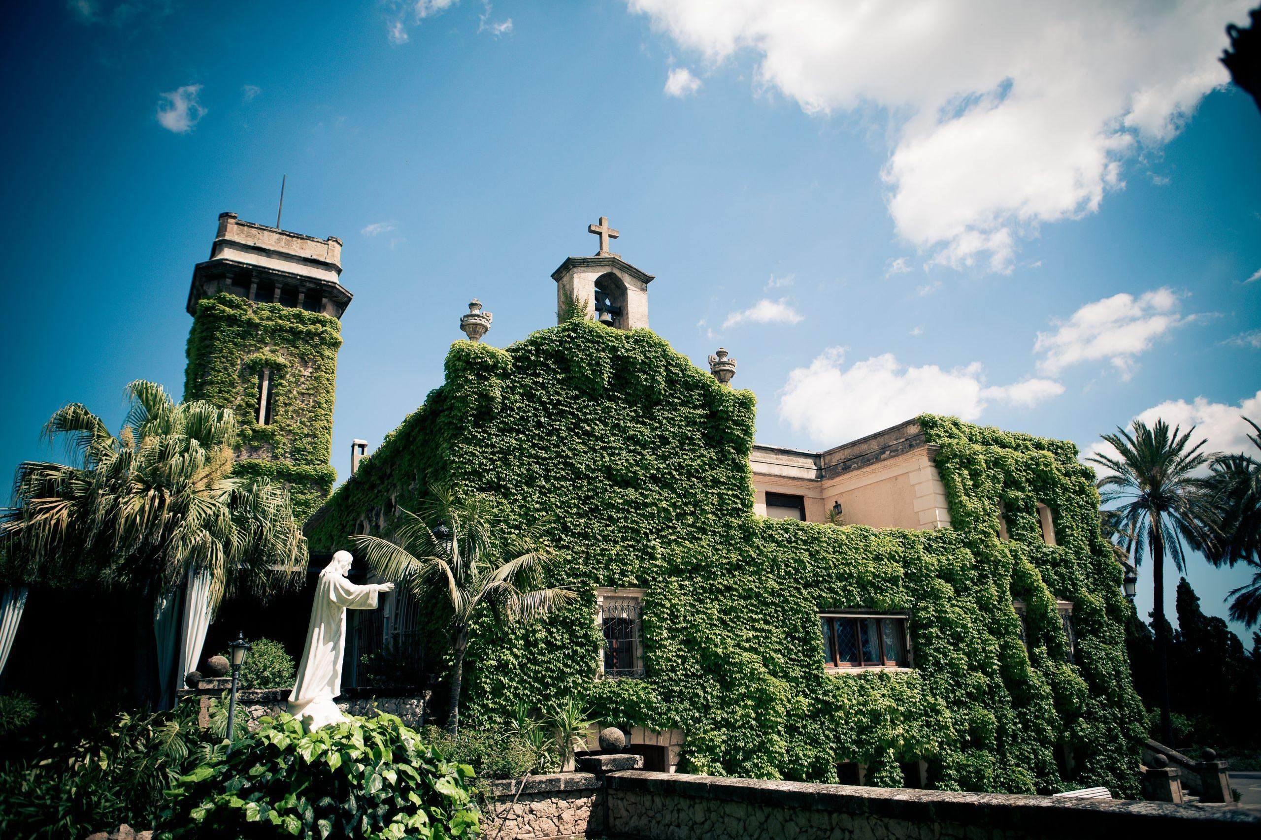 Ivy-covered façade and tower at Casa Santonja wedding venue, with a bell gable, garden statue and palm trees.