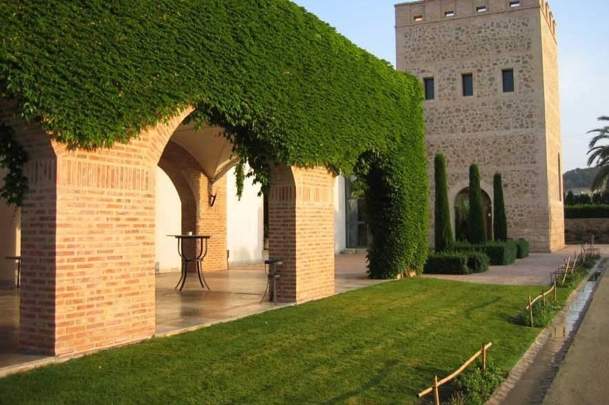 Ivy-covered brick arches beside a stone tower and lawn at Huerto de Santa María wedding venue.