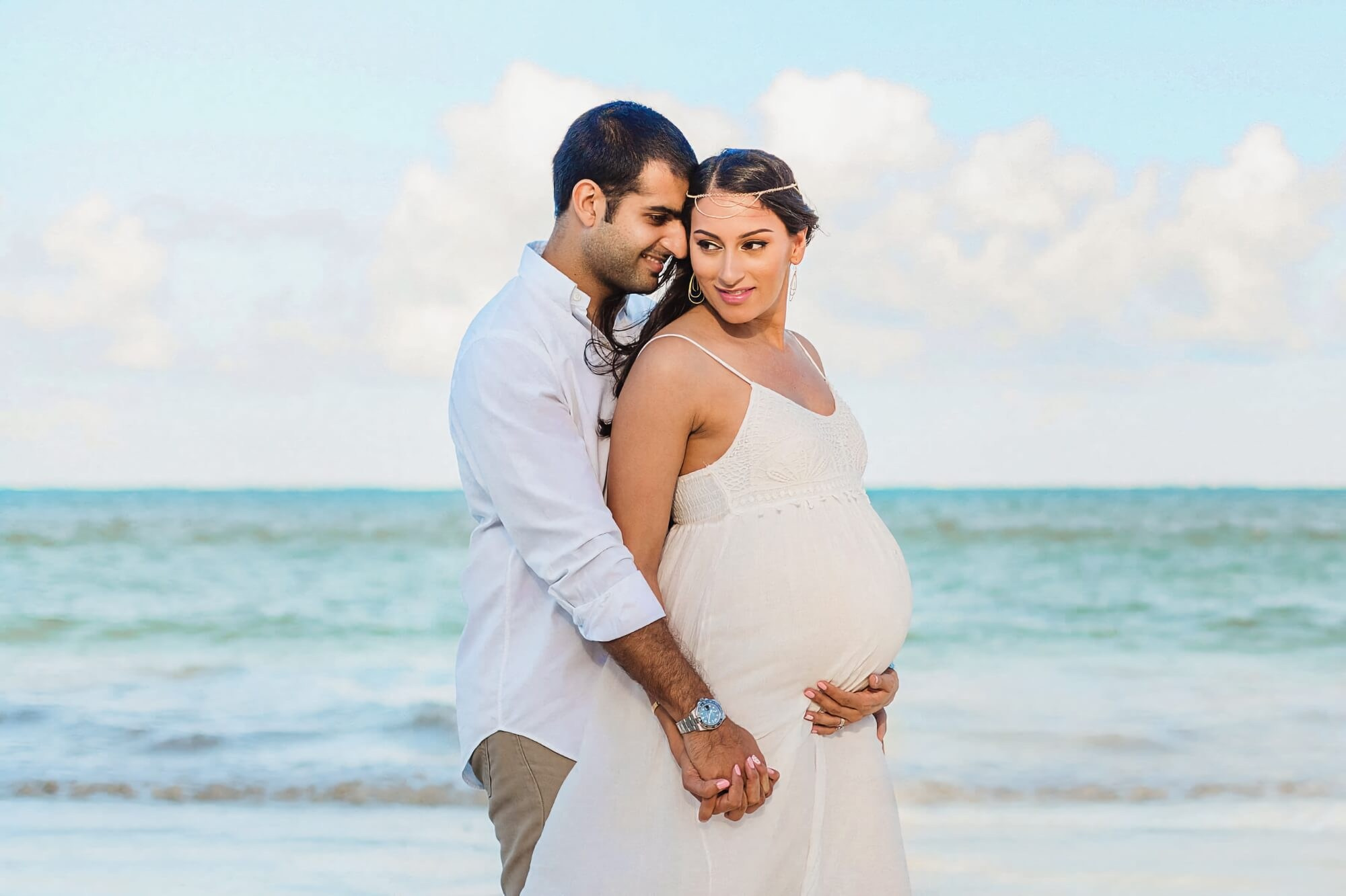 Young family smiling on the sand with the Indian ocean – Mombasa Kenya beach pregnancy maternity photography.