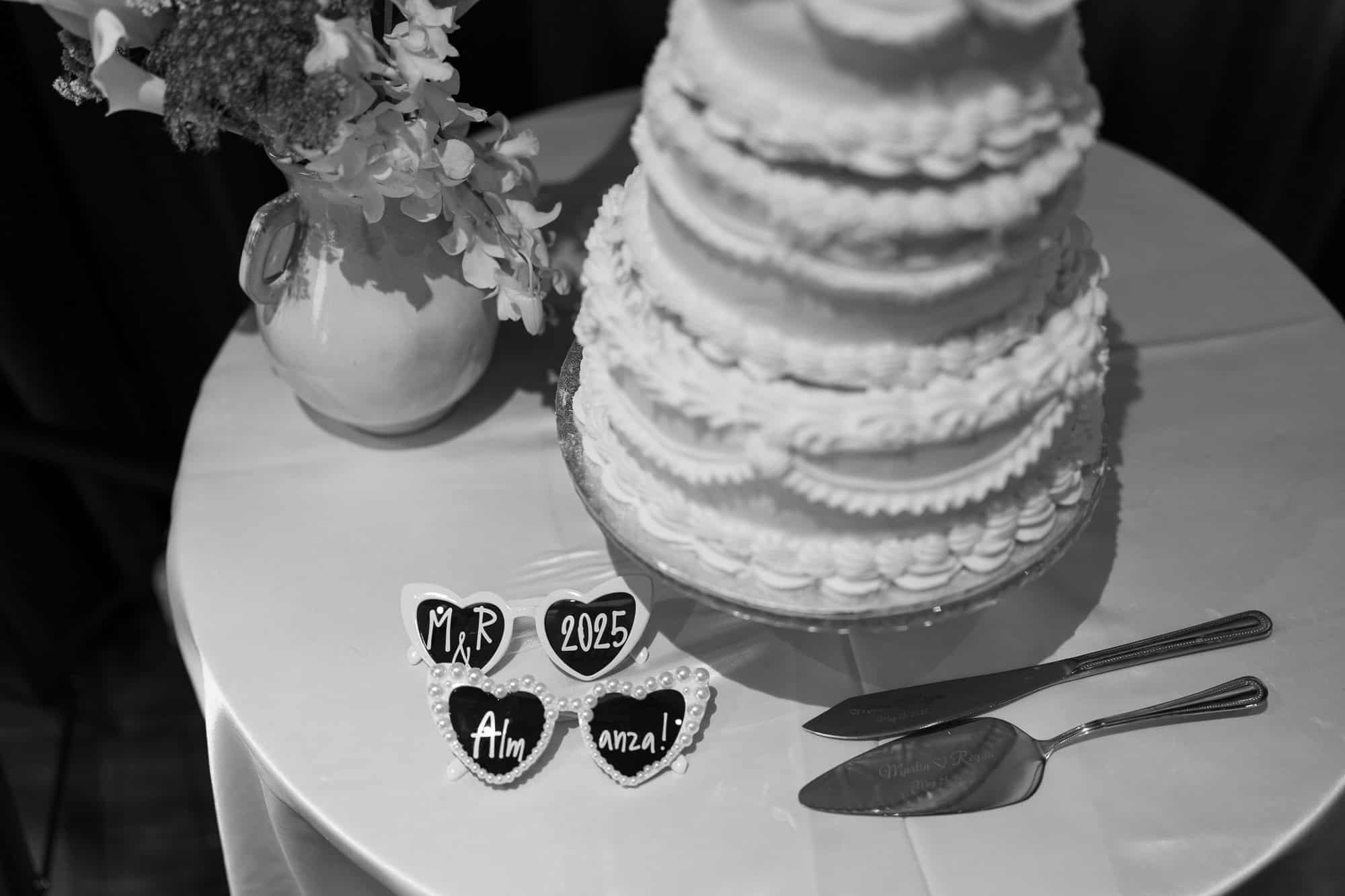 Close-up of wedding cake with floral decor and personalized heart-shaped glasses (black and white)