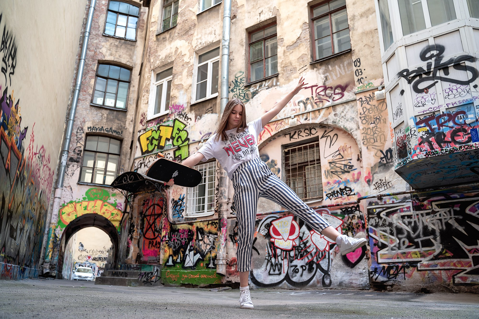 Young woman in shorts and a white t-shirt holding a skateboard, street fashion photo shoot in front of graffiti, commercial advertisement for youth clothing