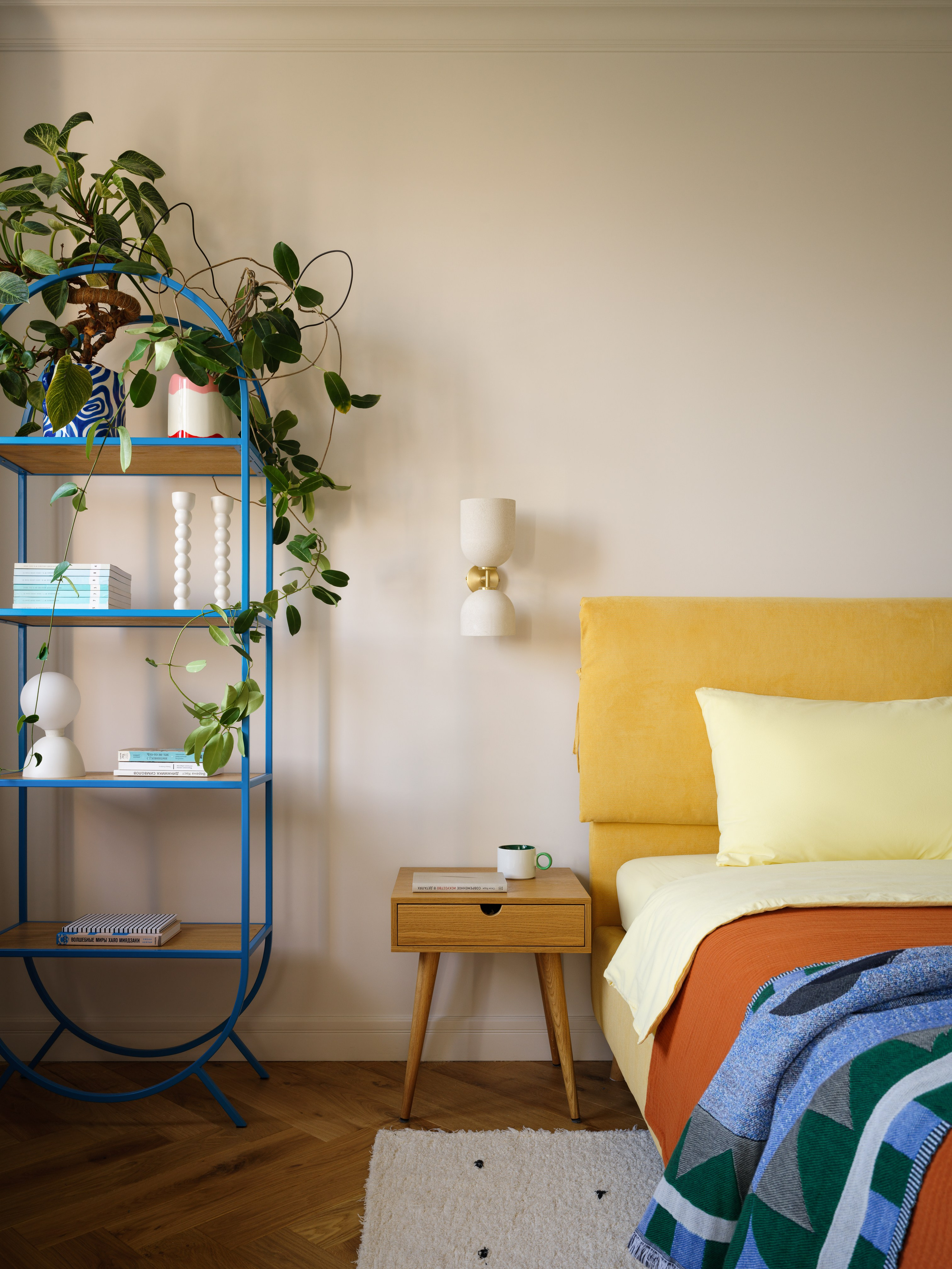 Интерьер спальни с ярко-желтой кроватью, рабочим местом у окна и металлическим стеллажом.