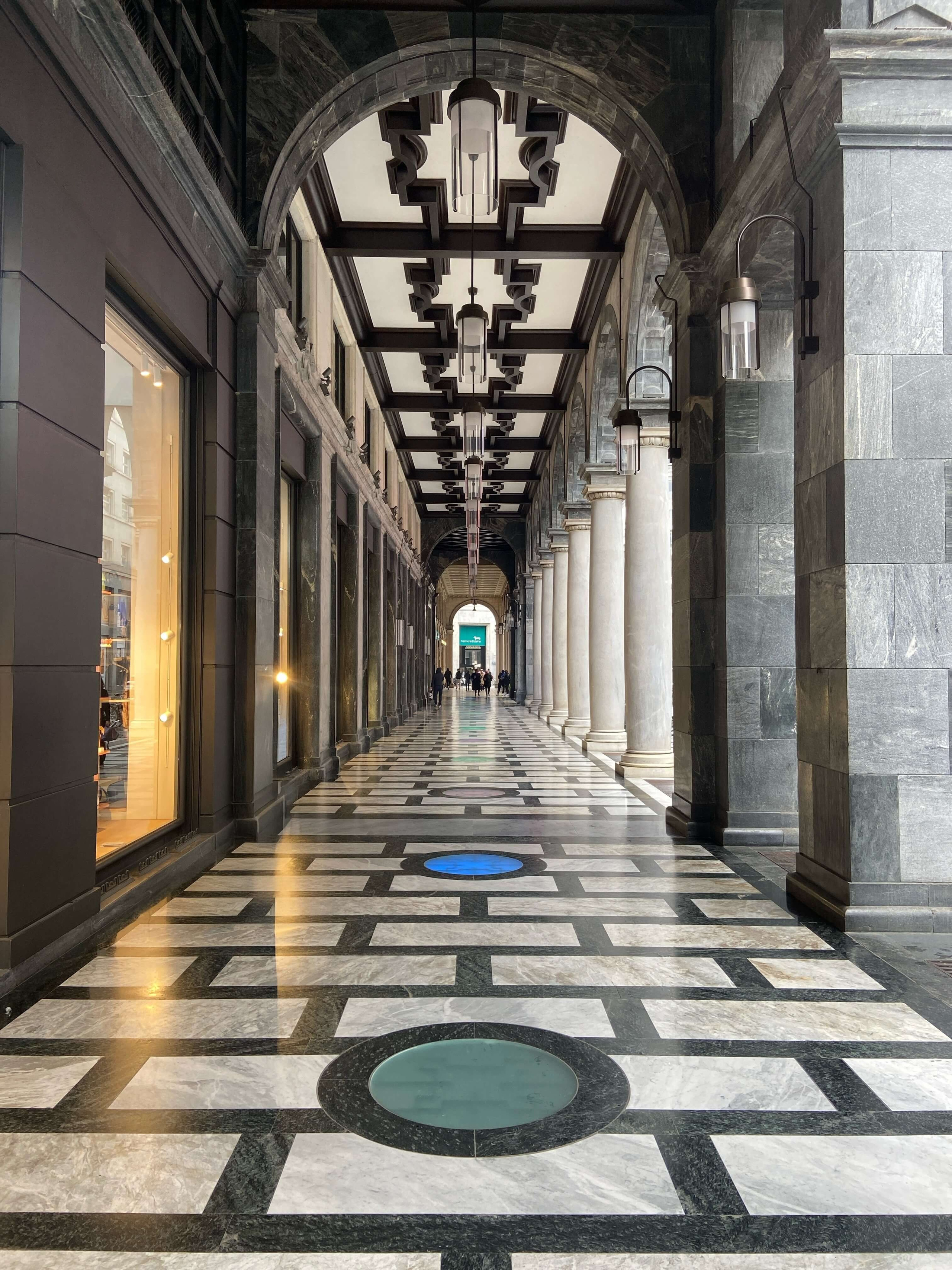 Arcade architecture with marble floor and luxury storefronts used as backdrop for fashion photoshoot in Milan
