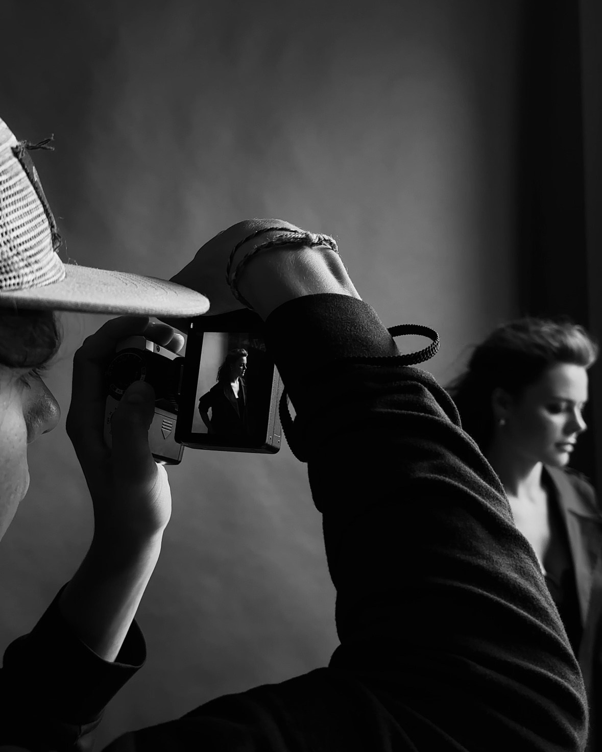 Black and white portrait of a woman with long braids leaning forward on a stool, gazing into the camera.