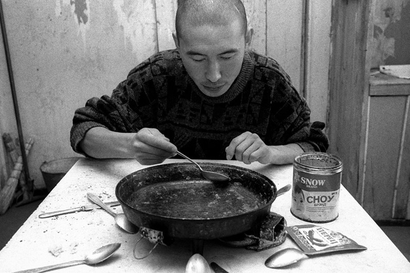 The young monk in charge of delivering the firewood is the last to arrive at the meal, and gets only what is left of the meal, Verkhnyaya Ivolga village, Buryatia, Russia. November 2001