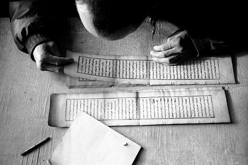 The monk bent over a prayer book, the text of which was written in the Mongolian language, Verkhnyaya Ivolga village, Buryatia, Russia. November 2001