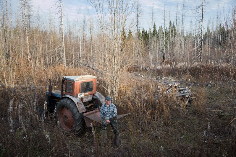 A man rests on his tractor while gathering firewood to heat his house in winter, Yuroma village, Leshukonsky district, Arkhangelsk region, Russia. 2021