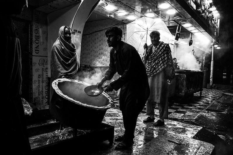 Street cooks pour excess fat from pilaf into a ditch, Shur Bazar, Kabul, Afghanistan. 2024
