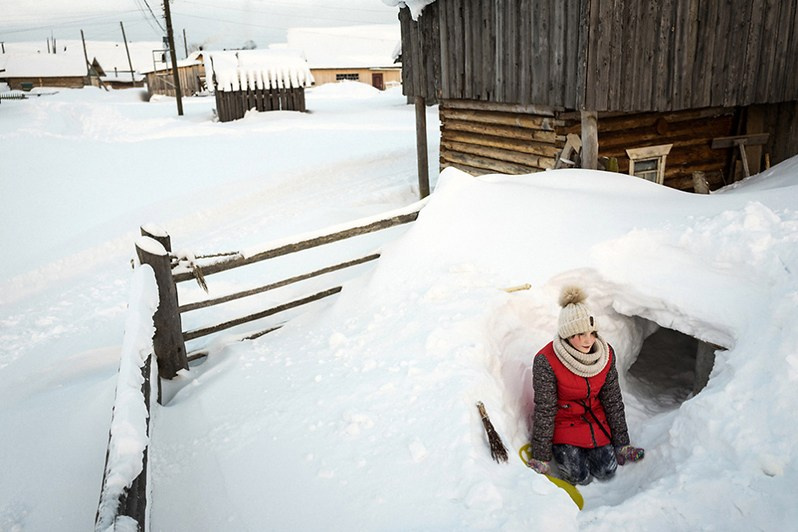 A girl plays in the snow in her home's backyard, Koynas village, Leshukonsky district, Arkhangelsk region, Russia. 2018