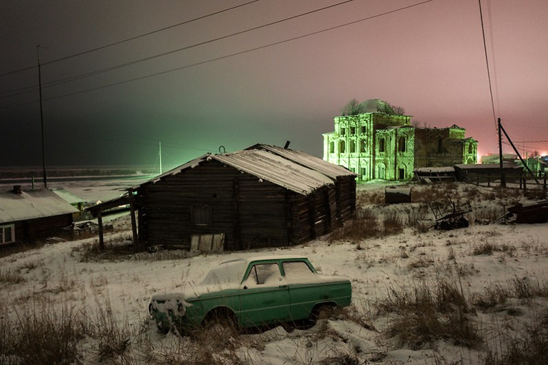 An abandoned car with the ruins of an old church in the background, Glotovo village, Udorsky district, Komi Republic, Russia. 2018