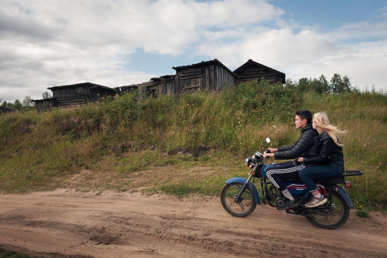 A boy and his girlfriend ride a motorbike along a country road, Vazhgort village, Udorsky district, Komi Republic, Russia. 2020