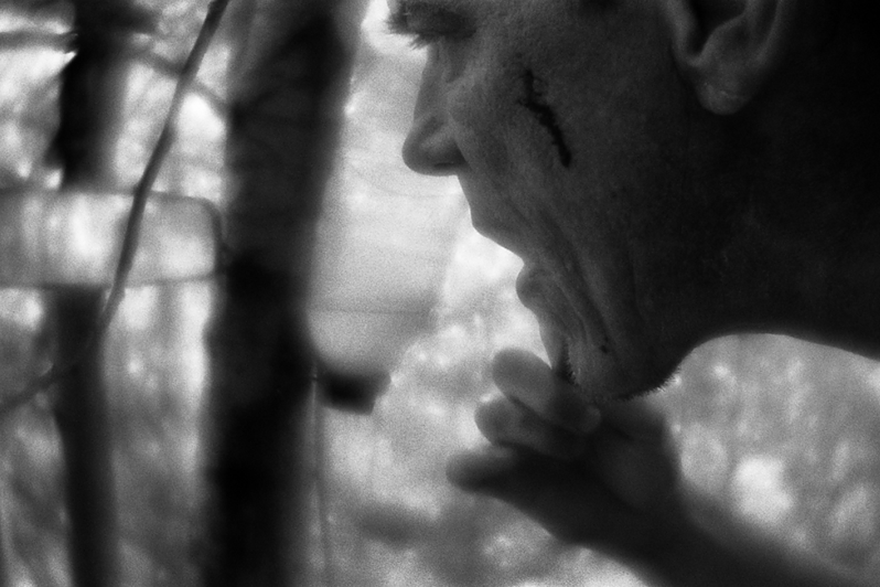 Костя бреется, глядя в зеркало заднего вида автомобиля, прикреплённое к дереву рядом с импровизированным умывальником, сделанным из перевёрнутой пластиковой бутылки для воды, район Тропарёво-Никулино, Москва, Россия. 12 июня 2015