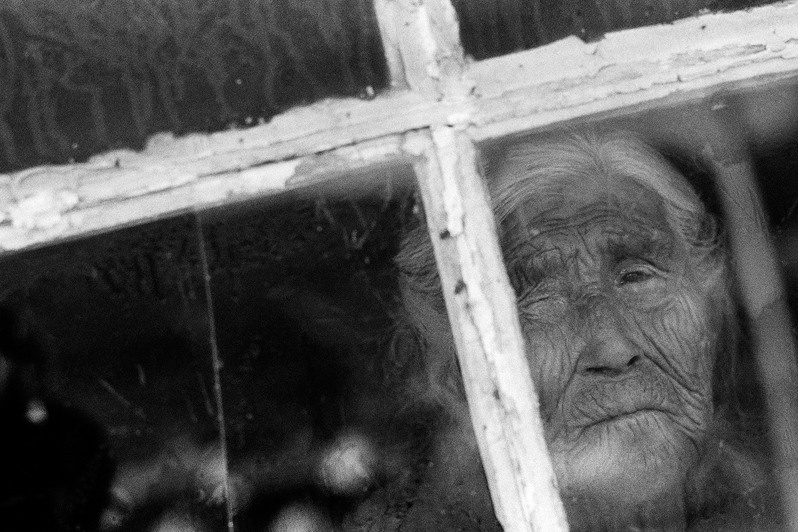 Old Woman peers through her window in Tasiusaq, Tasiusaq settlement, Kujalleq municipality, Greenland, Kingdom of Denmark. 1990