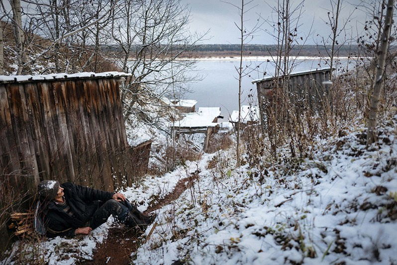 A man rests by a shed after having a drink, Leshukonskoe village, Arkhangelsk region, Russia. October 2017