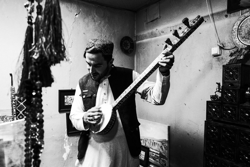 A young Afghan man demonstrates playing a national musical instrument, Kabul, Afghanistan. 2024