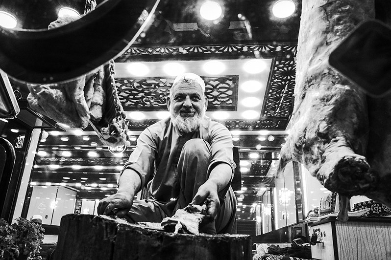 A butcher butchers a ram carcass sitting in a shop window, Shur Bazar, Kabul, Afghanistan. 2024
