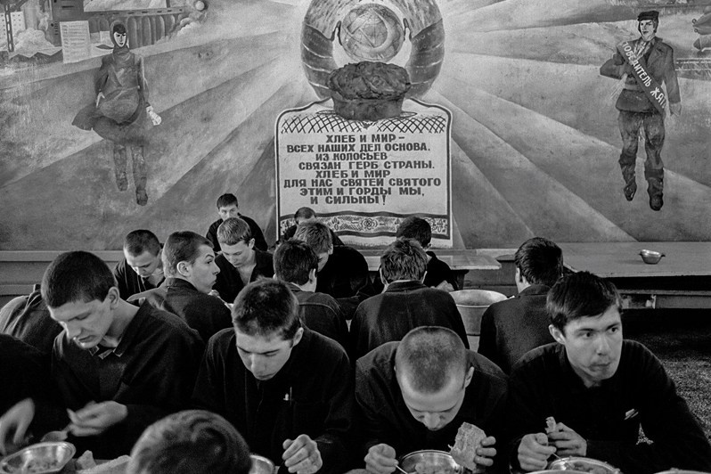 In the canteen of a specialized closed-type reform school (juvenile detention center) for teenagers aged 14 to 18, against the backdrop of a Soviet propaganda mural featuring a coat of arms, Raifa village, Zelenodolsk district, Tatar ASSR, USSR. 1989 © Oleg Klimov