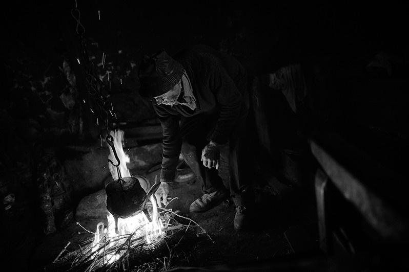 Man lights a fire indoors to heat his food, Montalegre municipality, Vila Real district, Trás-os-Montes region, Portugal. 2017