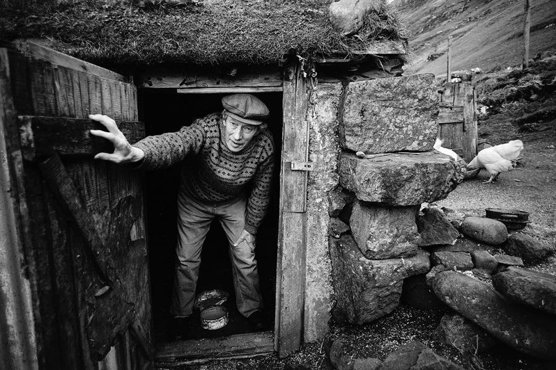 Per Hansen coming out of the hen house with a tin of poultry feed, Tjörnuvik village, Sunda municipality, Faroe Islands, Kingdom of Denmark. 1987