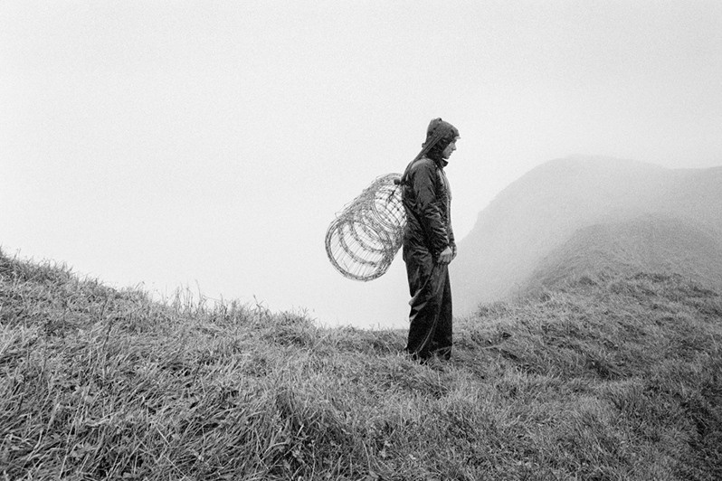 Elias Nes with a bundle of wire behind his back on a hill in Mykines Island, near Mykines village, Sørvagur region, Faroe Islands. 1996