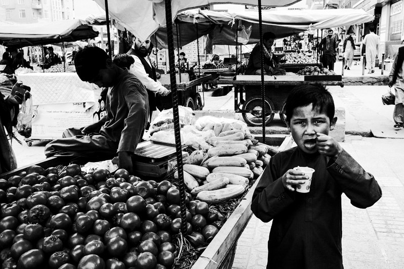 A boy eats fruit at a market, Mazar-i-Sharif, Balkh province, Afghanistan. 2024