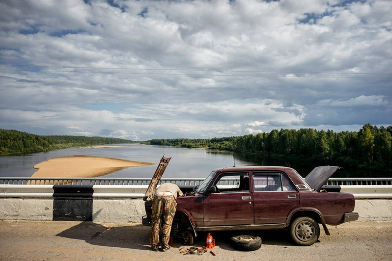 A man repairs his car on a bridge over the Mezen River, near Usogorsk urban-type settlement, Komi Republic, Russia. August 2017