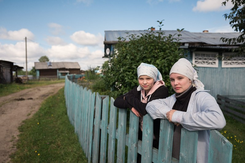 Sisters Lera and Katya leaning on the fence of their house, Vazhgort village, Udorsky district, Komi Republic, Russia, 2020