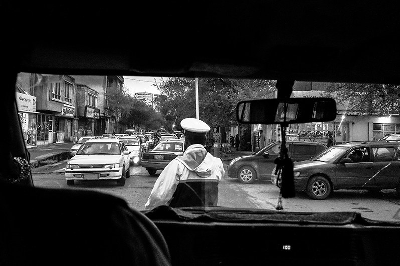 A traffic controller at an intersection directs traffic and redirects suspicious vehicles to the Taliban for inspection, Kabul, Afghanistan. 2024