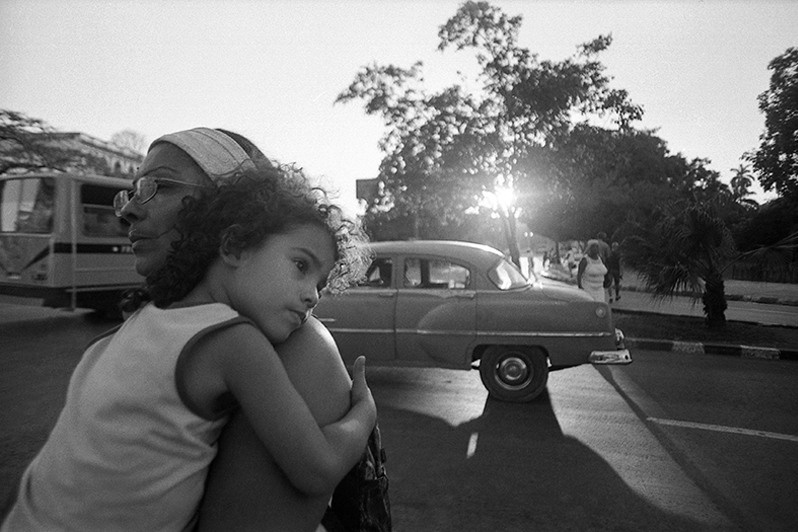 Mother carries her daughter in her arms as she crosses a street in the centre of Havana, Fraternity Park, Centro Habana district, Havana, Cuba. 2017