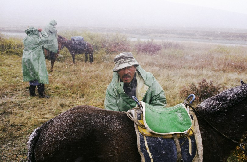 Saddling horses in the increasing wind and snow, Ulaan Taiga mountains, Khövsgöl province, Mongolia. September 2009