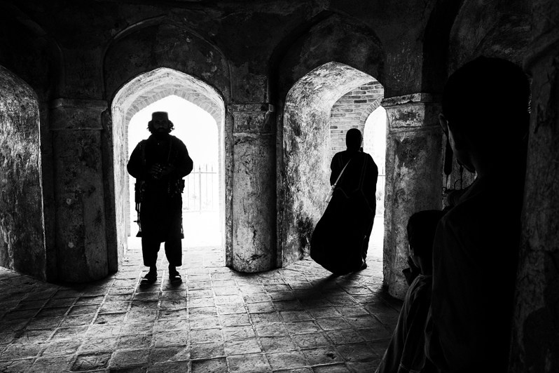 A Talib guard keeps a watchful eye out and keeps the local population away from a foreign woman, Balkh, Afghanistan. 2024