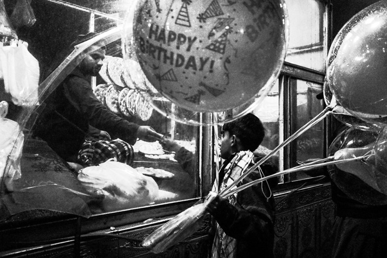 A boy with balloons buys bread on his birthday, Kabul, Afghanistan. 2024