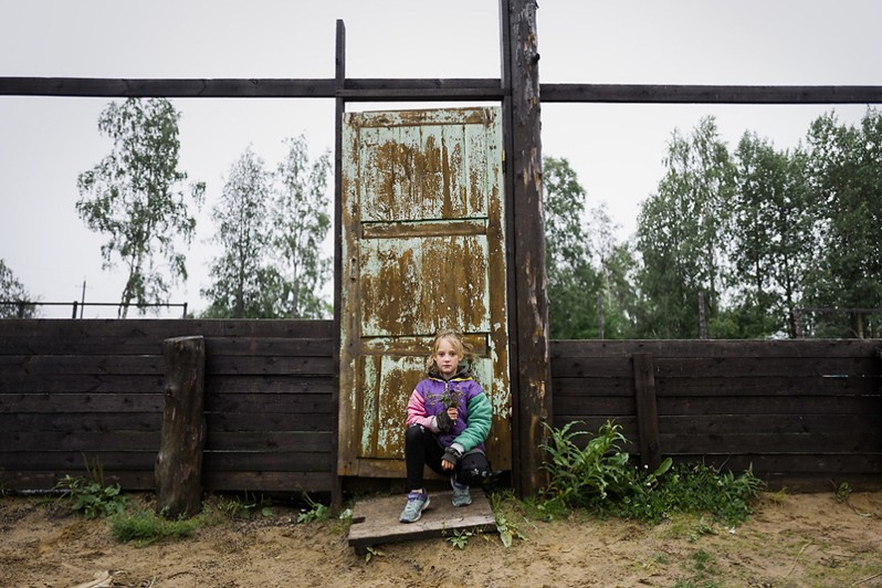 A girl with a bouquet of flowers sits in front of the entransce to the playground, Kamenka village, Mezensky district, Arkhangelsk region, Russia. 2019