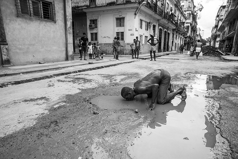 Scene of a mentally ill man drinking water from a puddle in the centre of Havana, Centro Habana district, Havana, Cuba. 2016
