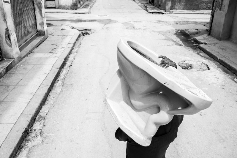 Surreal episode of a man carrying a toilet bowl through the streets of the Los Sitios neighbourhood, Centro Habana district, Havana, Cuba. 2020