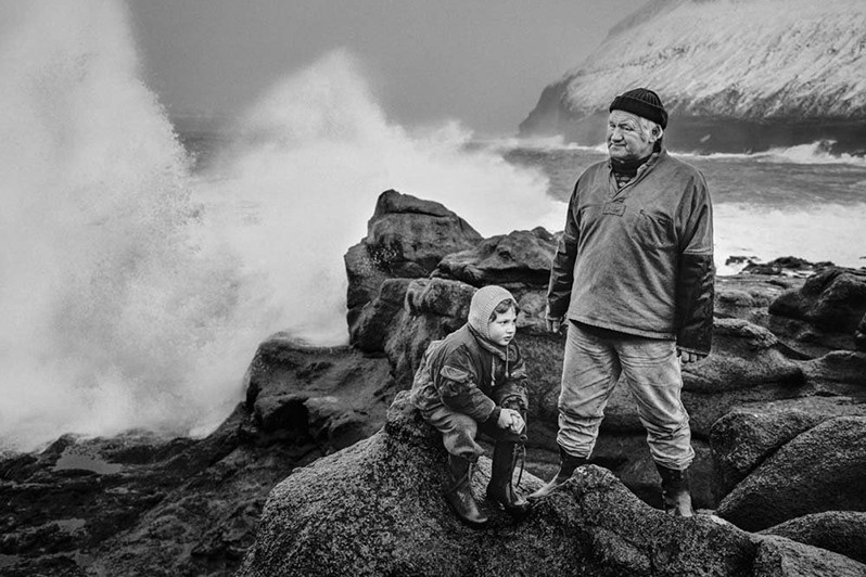 Poul Sigurd Cristiansen stands by the sea in a raincoat with his grandson, Gjogv village, Nordoyar region, Faroe Islands, Kingdom of Denmark. 1988