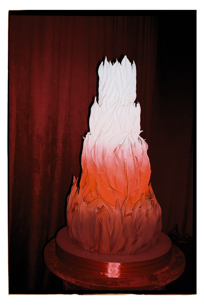 Wedding cake displayed against red backdrop during luxury reception