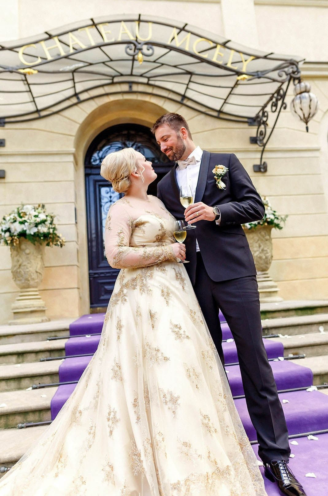 Stylishly dressed newlyweds share a champagne toast in front of the a historic chateau in the Czech Republic.