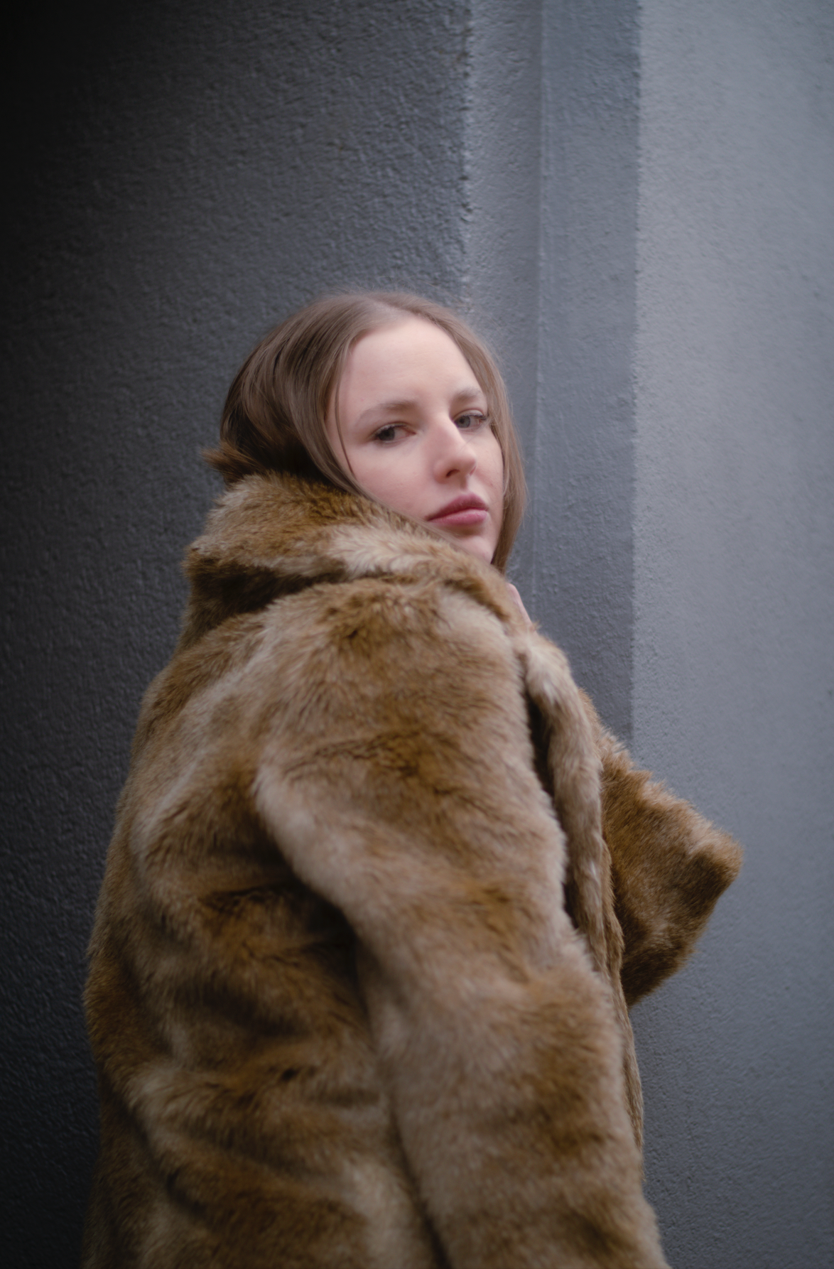 Porträt einer jungen Frau mit dunkelblonden Haaren, blauen Augen und Faux-Fur Mantel vor einem blau-grauem Hintergrund