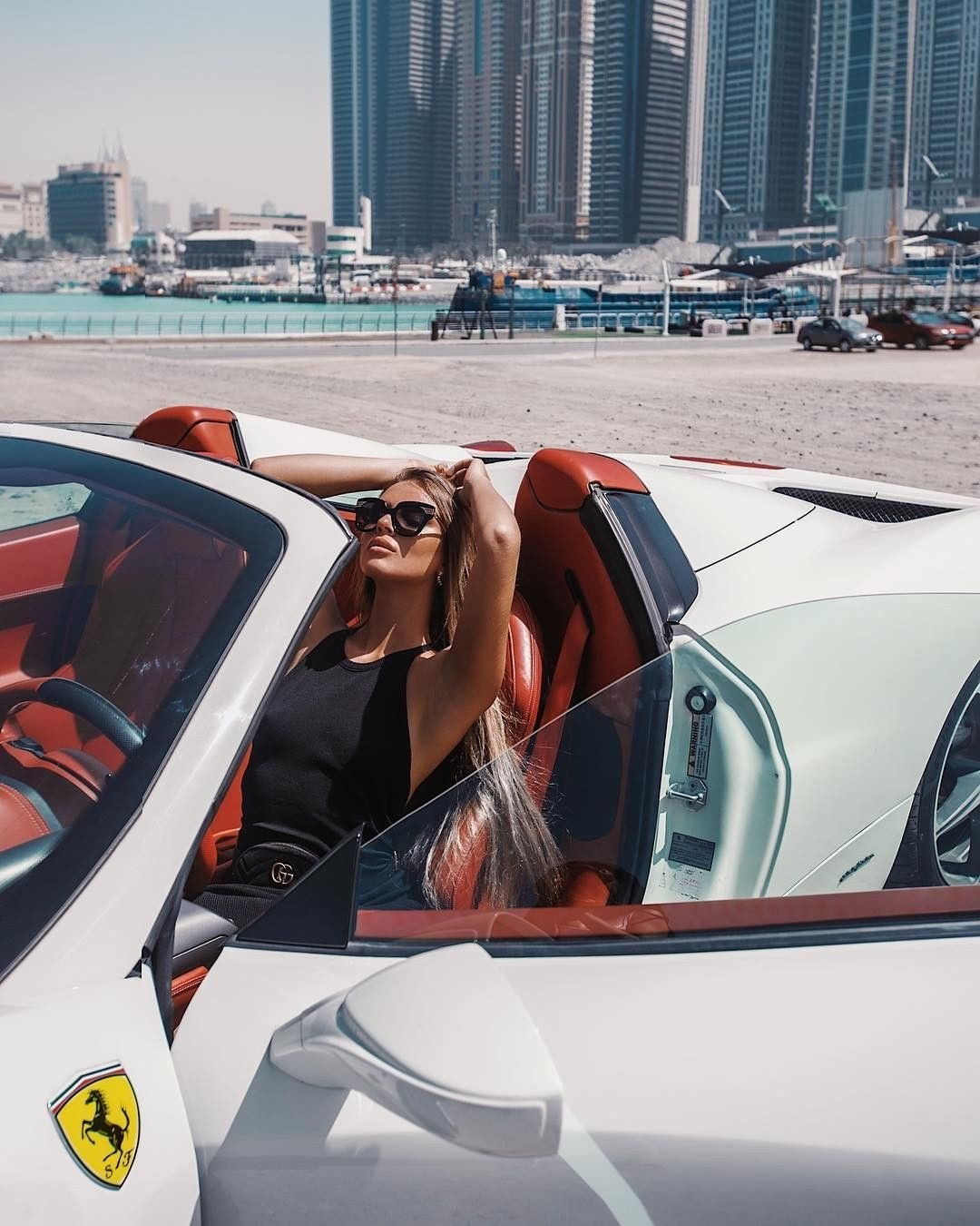 A model-looking girl sits in the cabin of an expensive white Ferrari car against the backdrop of Dubai skyscrapers