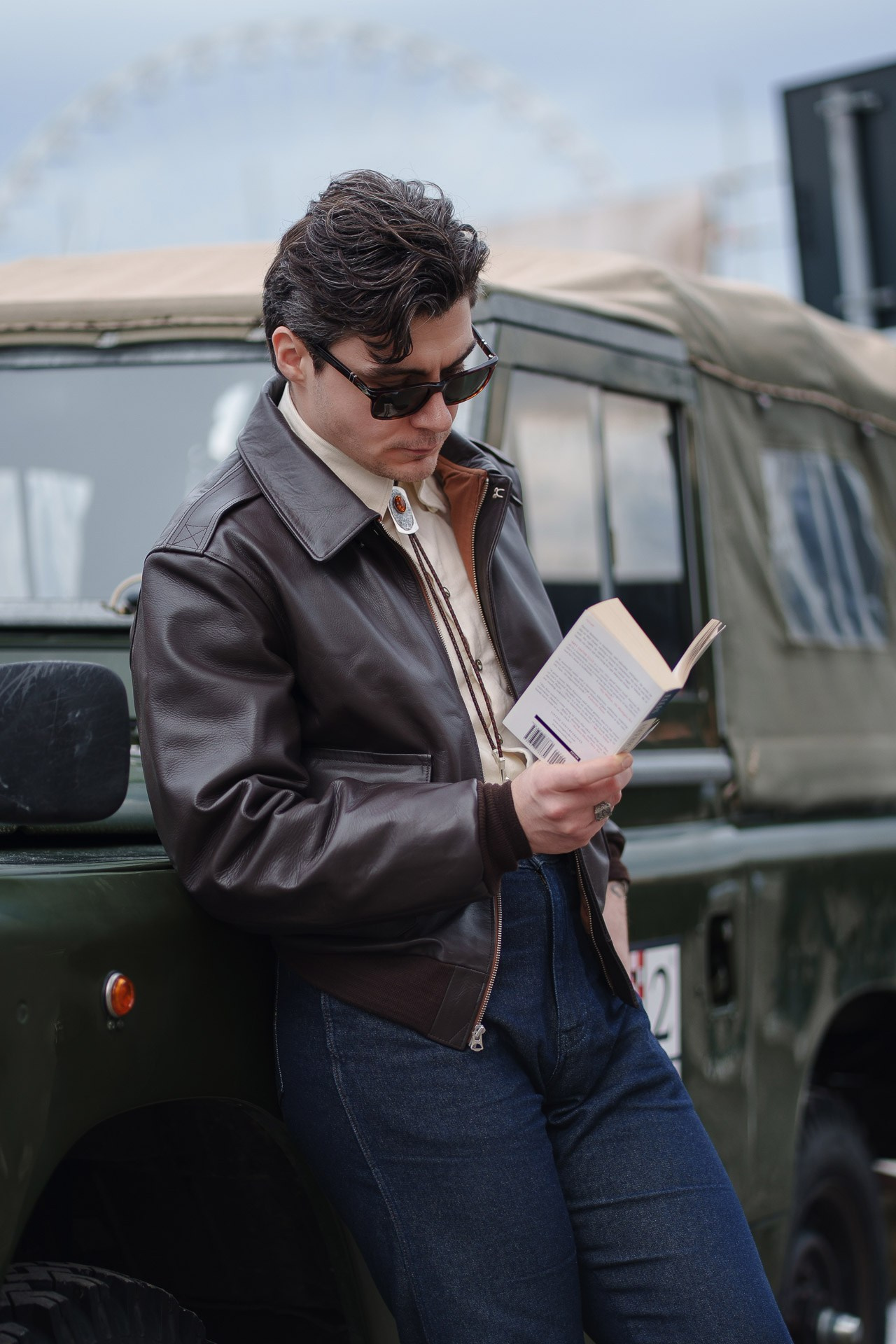 Man in leather jacket reading book near vintage car at Pitti Uomo 109 Florence