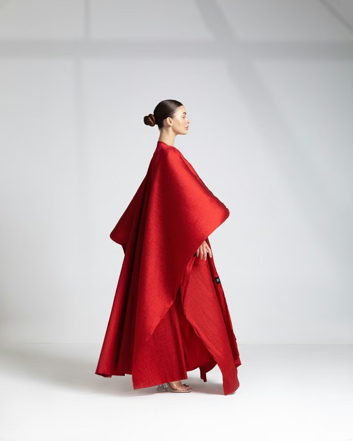Model wearing an elegant red draped garment, posing in profile with minimalist lighting